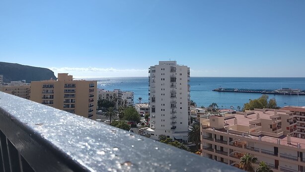 A coastal cityscape with a prominent white building, a clear blue sky, and a calm sea. - 'Achacay Beach' Holiday Apartment with Sea View, Pool and Wi-Fi (Los Cristianos)