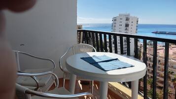 En balkon med et bord og stole, ud til et kystlandskab med bygninger og en bro.