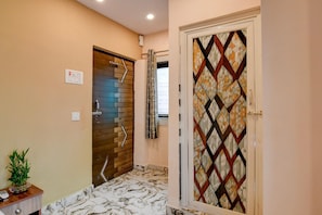 Un baño con piso de mármol, puerta de madera y puerta de vidrio con diseño geométrico.