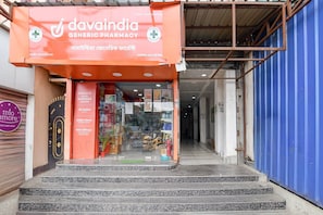 Una farmacia llamada 'davaindia generic pharmacy' con un cartel en varios idiomas, una puerta de cristal de entrada y una escalera que conduce a la entrada.