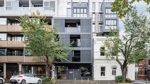 Ein mehrstöckiges Gebäude im modernen architektonischen Stil, mit einer Fassade aus Glas und Beton sowie einem baumbewachsenen Eingangsbereich.
