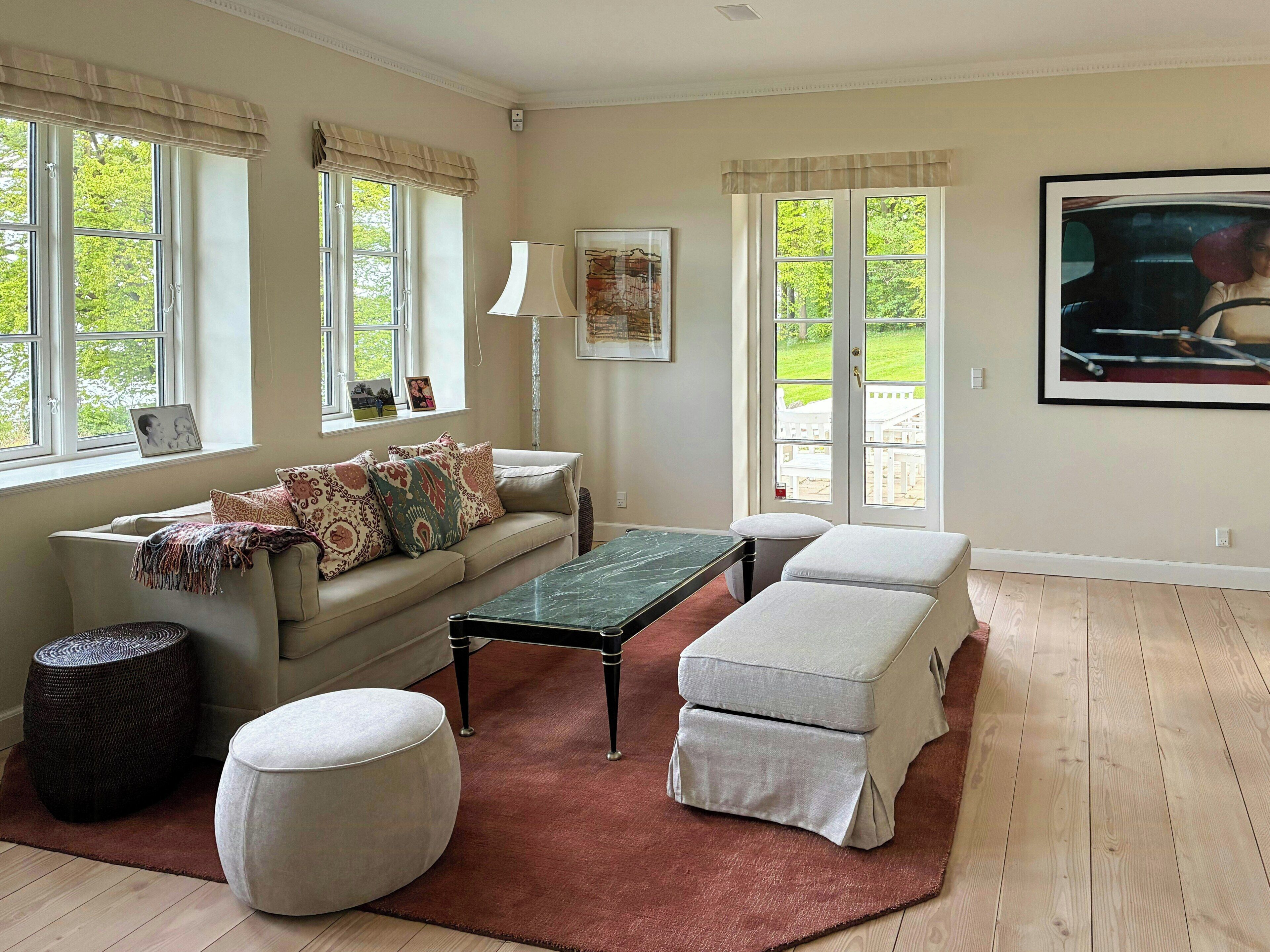 A living room with a sofa, ottoman, coffee table, and a large window with curtains.