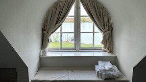 Quarto com janela, cama e vista para a água.