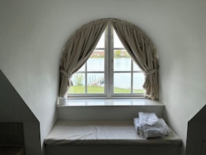Quarto com janela, cama e vista para a água.