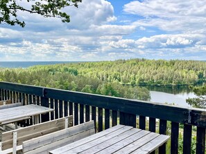 Eine Holzdielen-Terrasse mit Bänken, die auf einen See mit dichter Uferbewaldung blickt.