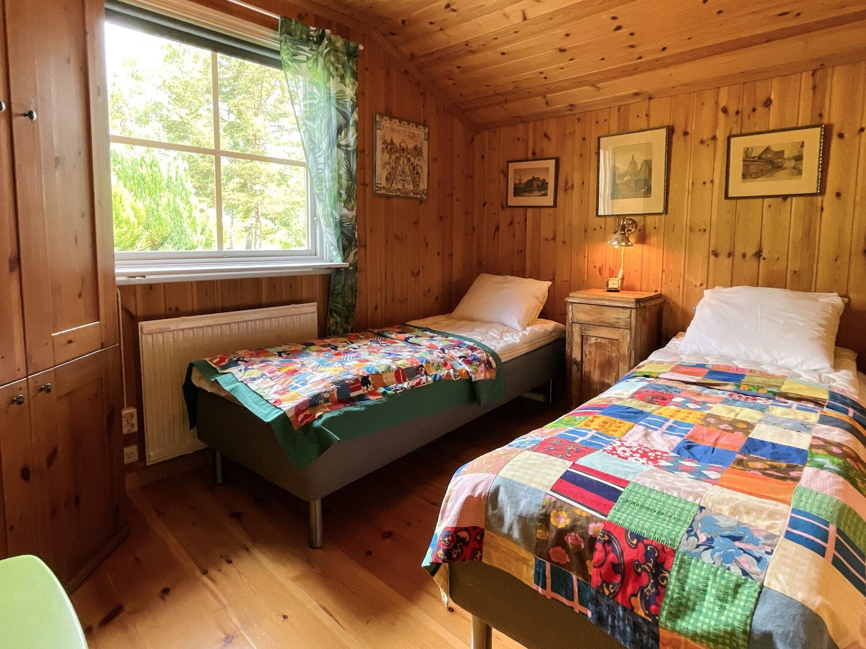 A cabin with two beds, a window with curtains, wooden walls, and a radiator.