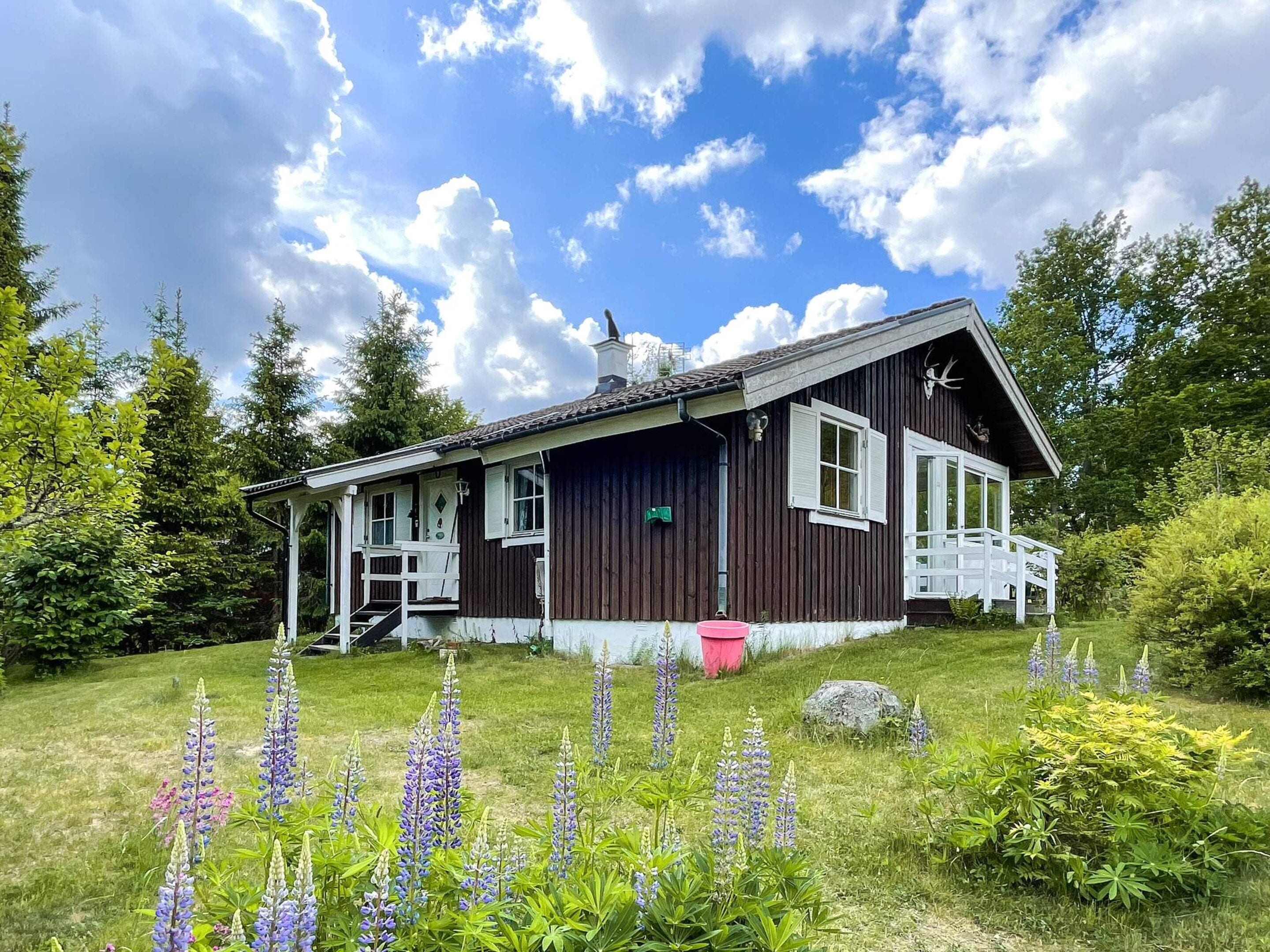 A wooden house with a porch, surrounded by a garden with purple flowers.
