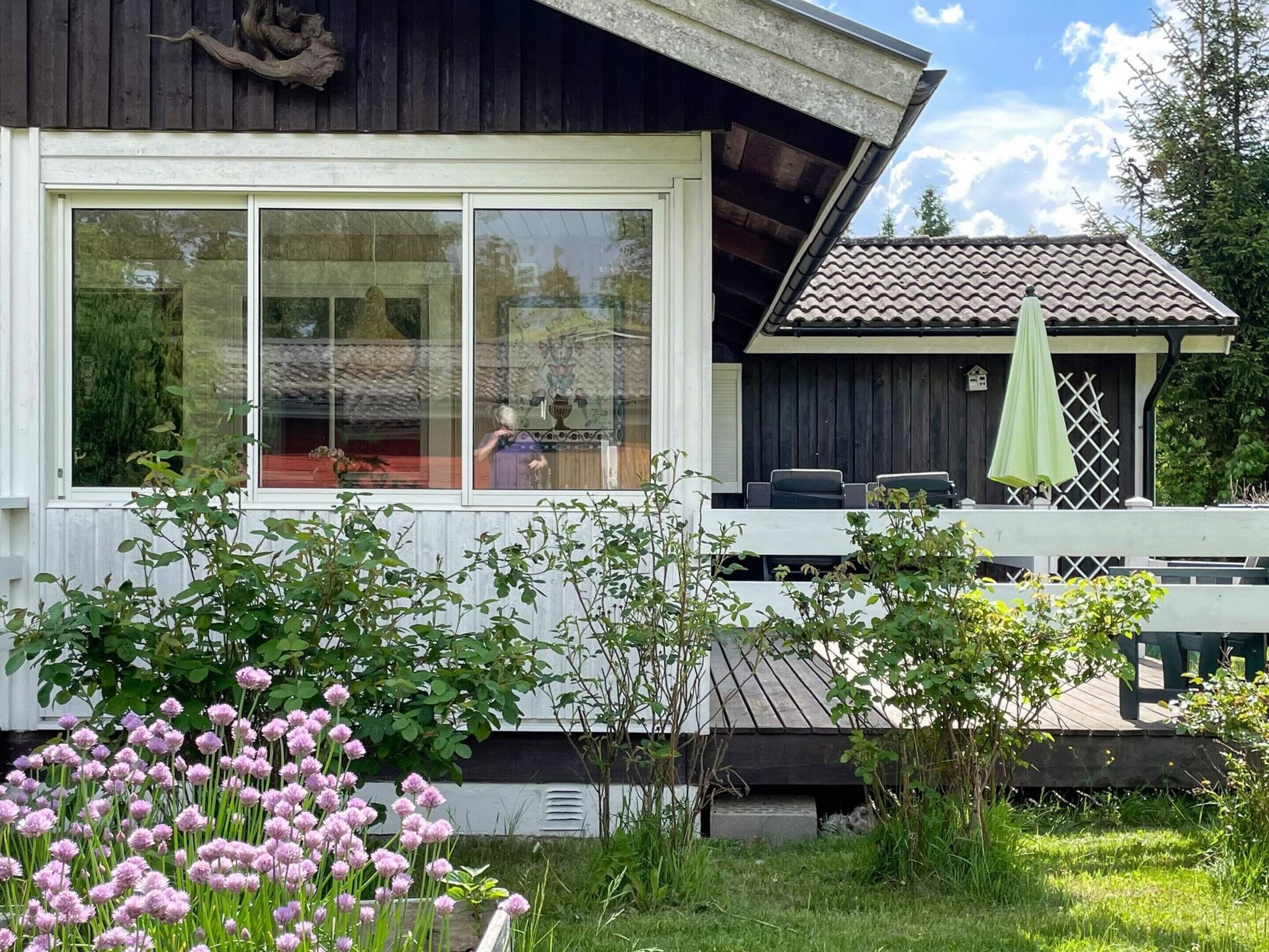 A wooden house with large windows, a balcony, and a green umbrella.