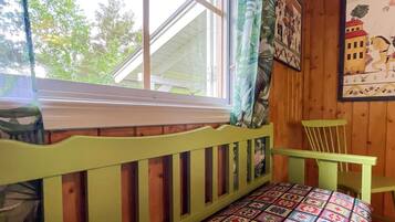 A room with a window, a green chair, a quilted bedspread, and a wall with a framed picture.