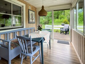 Eine überdachte Veranda mit Tisch und Stühlen, einer Hängeleuchte und Blick ins Freie.