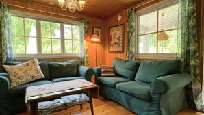 Una habitación acogedora con dos sofás verdes, una mesa de madera y ventanas grandes con cortinas.