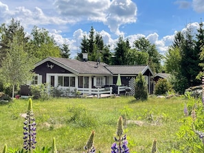 Eine rustikale Holzhütte mit Veranda, umgeben von üppiger Vegetation und Wildblumen.