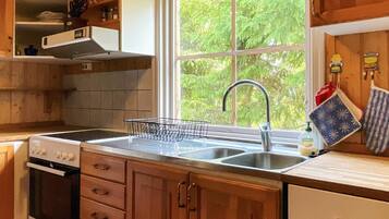 A kitchen with wooden cabinets, a stainless steel sink, a window with a view of greenery, and a dish rack.