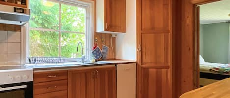 A compact kitchen with wooden cabinets, a built-in oven, and a window providing a view of greenery outside.
