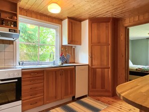 Cocina compacta con armarios de madera, horno empotrado y ventana con vistas a la vegetación.