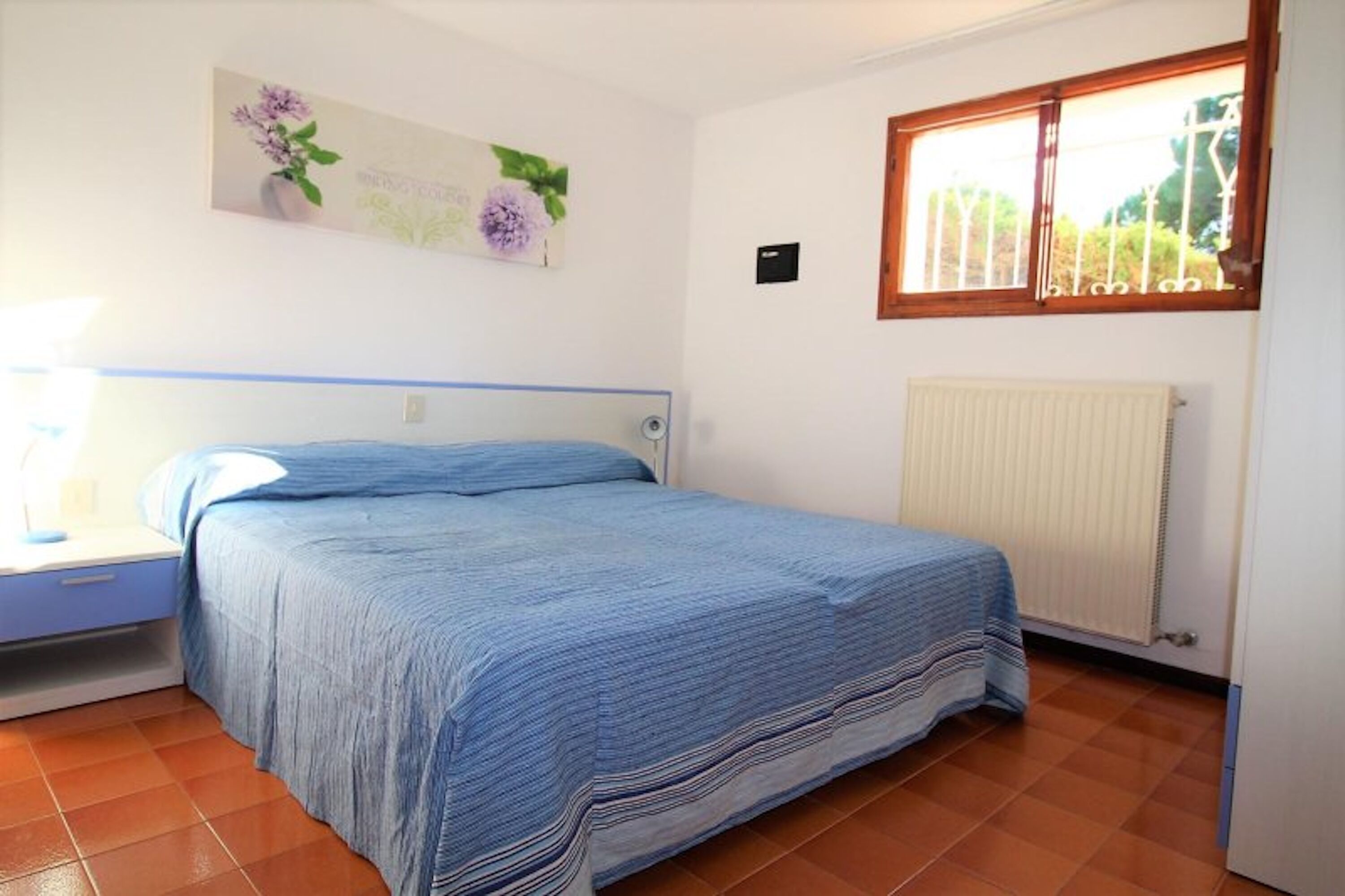 Un dormitorio con cama, mesita de noche, radiador y ventana con vista a zonas verdes.