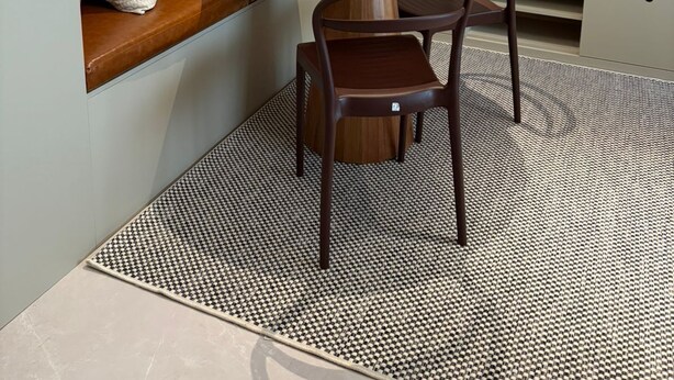 Un comedor moderno con una mesa redonda de madera, dos sillas, un banco con cojines, un espejo grande y un tapiz estampado.