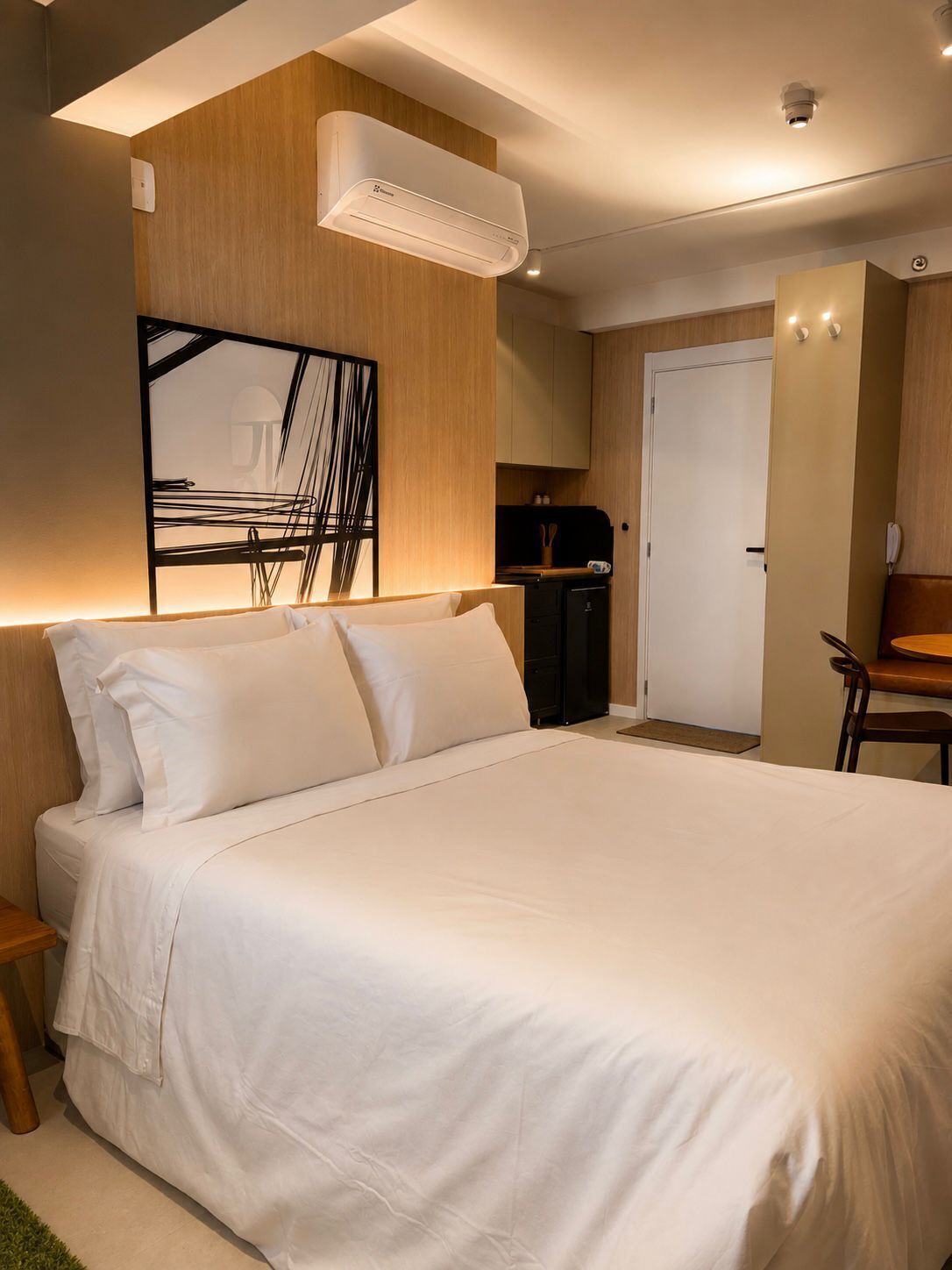 A modern bedroom with a large bed, a wall-mounted air conditioner, a wooden cabinet, and a door leading to a bathroom.