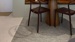 Un interior moderno con un sofá de cuero marrón, dos sillas de madera, una mesa redonda de madera, arte abstracto en la pared y una puerta de color claro.