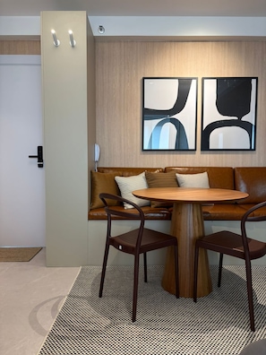 Ein modernes Interieur mit einem braunen Ledersofa, zwei Holzstühlen, einem runden Holztisch, abstrakten Wandbildern und einer hellen Tür.