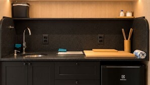 Una cocina moderna con un lavamanos integrado, un refrigerador compacto y una encimera con tabla de cortar y utensilios.