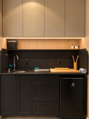 Eine moderne Küche mit integriertem Spülbecken, einem kompakten Kühlschrank und einer Arbeitsplatte mit Schneidebrett und Küchenutensilien.