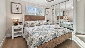 Une chambre à coucher avec un grand lit, une table de chevet, une lampe, un miroir et des œuvres d’art encadrées accrochées au mur.