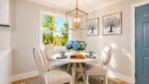 Un coin repas avec une table ronde, quatre chaises, un vase de fleurs et des œuvres d’art encadrées accrochées au mur.