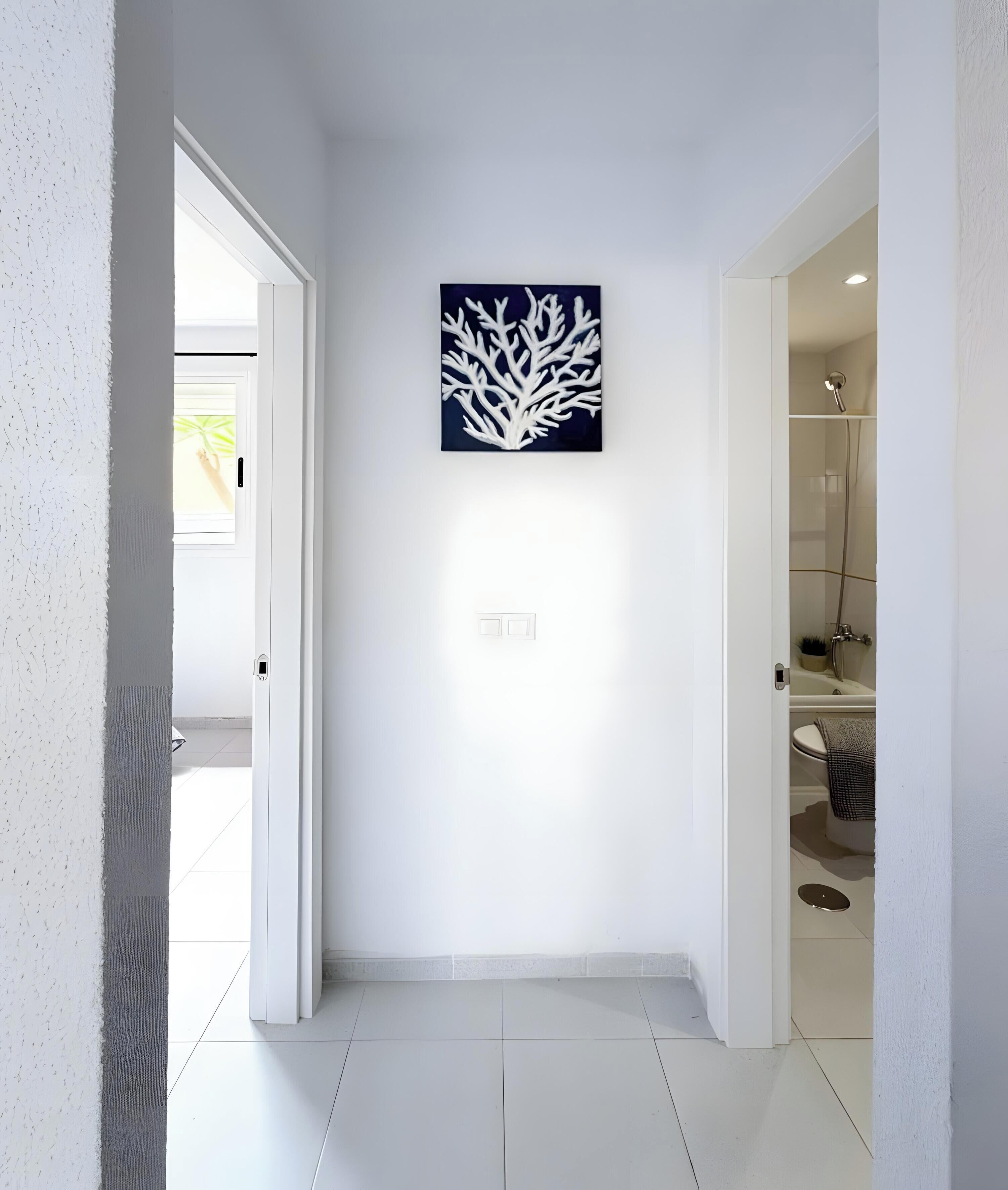 A hallway with a white door, a wall-mounted artwork, and a bathroom visible through an open door.