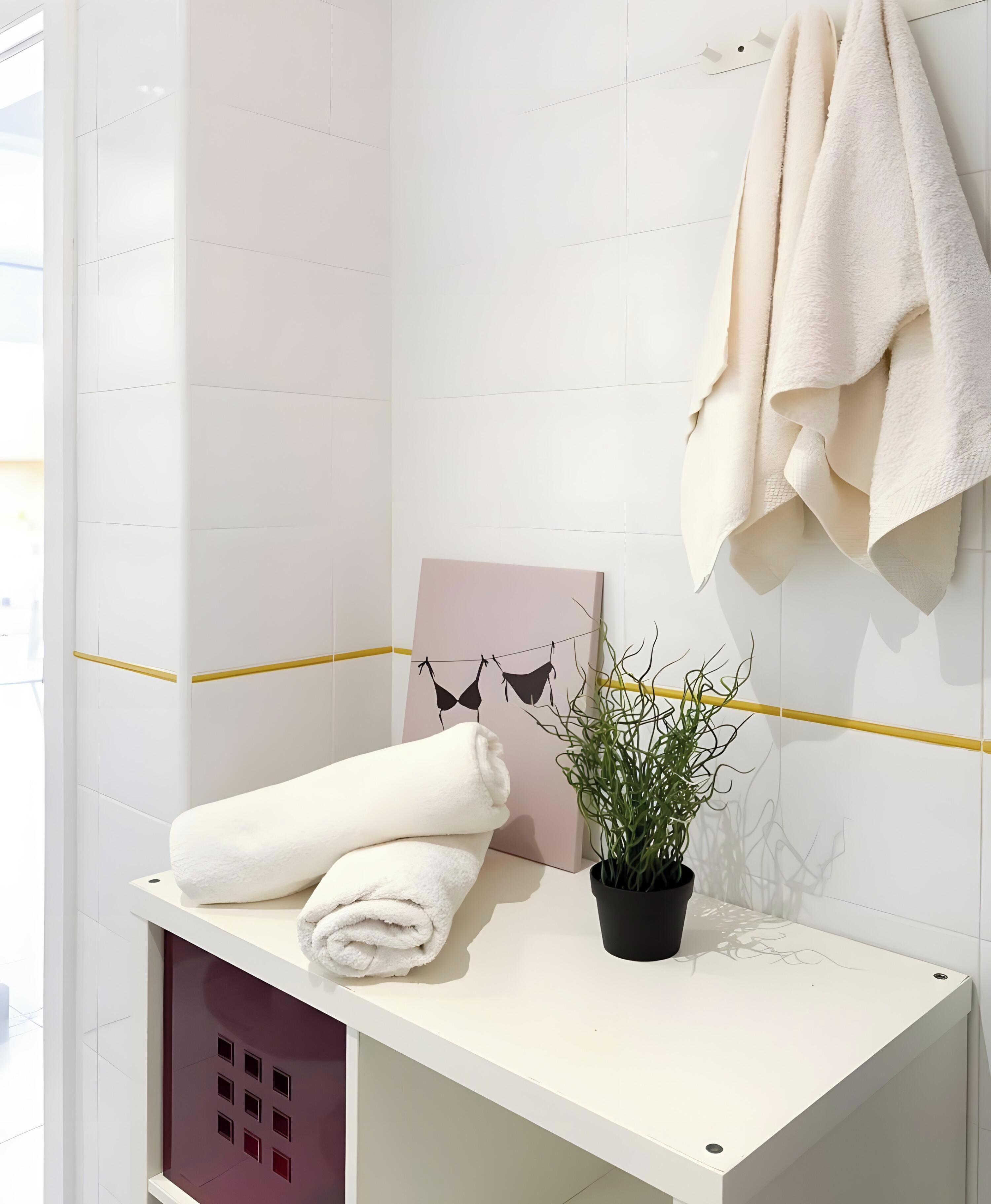 A bathroom with a white vanity, a towel, a potted plant, and a towel rack.