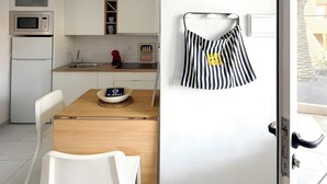 Eine moderne Küche mit weißen Schränken, einer Mikrowelle und einem Kühlschrank. Ein Esstisch mit einem weißen Stuhl und ein gestreiftes Handtuch an der Wand.
