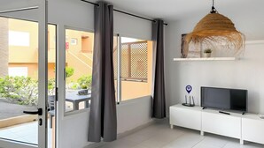 Ein modernes Wohnzimmer mit Fernseher, weißem Schrank und Blick auf einen Balkon mit Pflanzen.