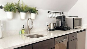 Eine moderne Küche mit Spüle aus Edelstahl, einer Kaffeemaschine, einer Mikrowelle und Topfpflanzen an der Wand.