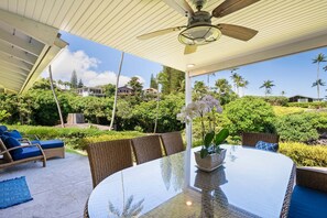 Eine Terrasse im Freien mit einem Glastisch, Korbmöbeln und einem Deckenventilator.