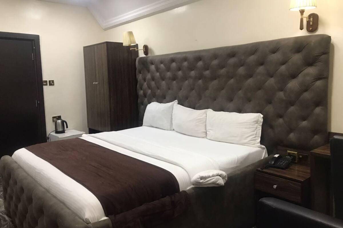 Habitación de hotel con una cama grande, un armario, una mesita de noche con lámpara y un teléfono.