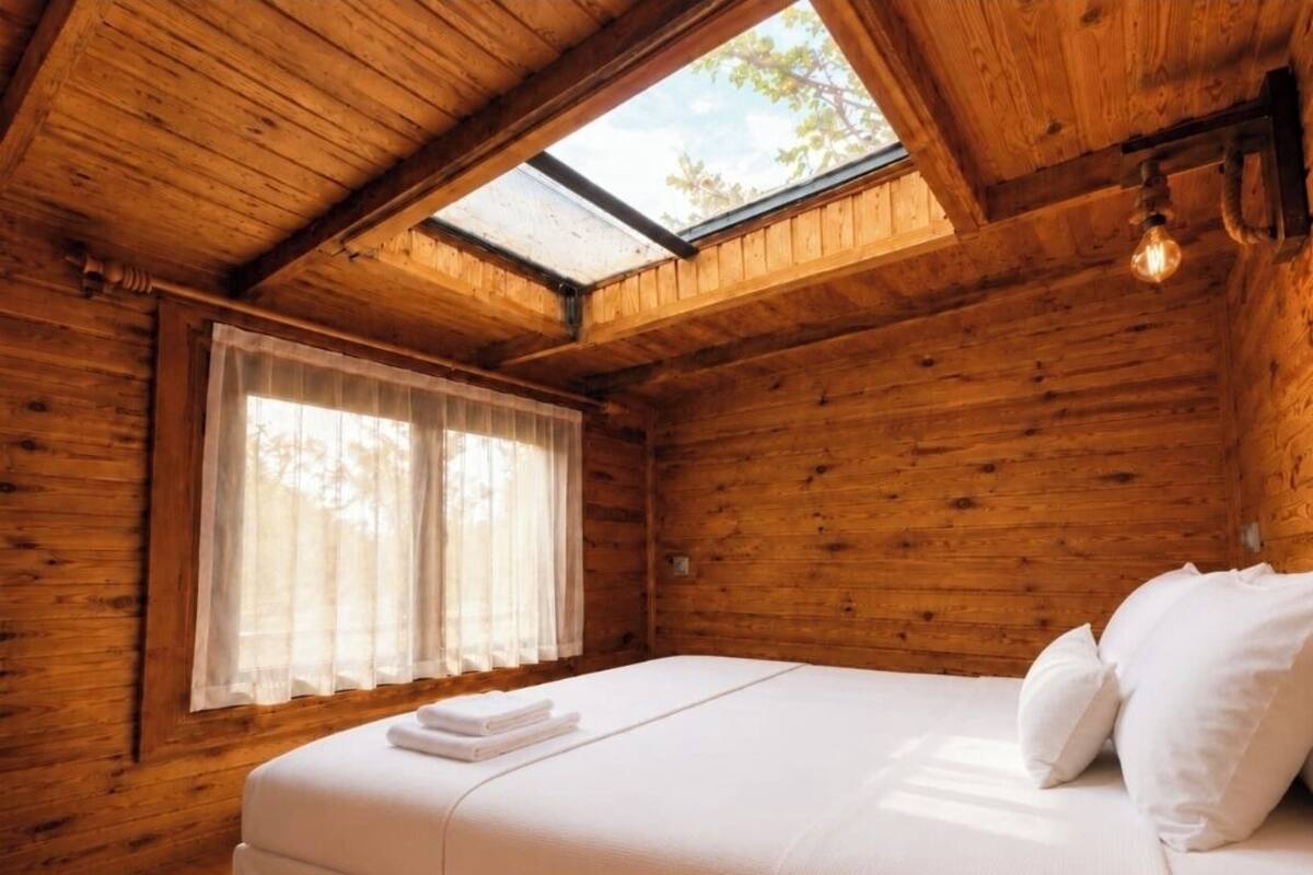 Una camera in una baita di legno, con un letto, un lucernario e una finestra con tende.