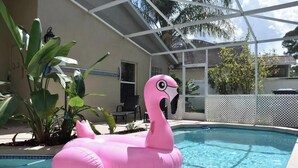 A swimming pool with a pink flamingo float, surrounded by plants and a covered patio area. - 4 Bedroom Modern Pool home close to UCF (Oviedo)