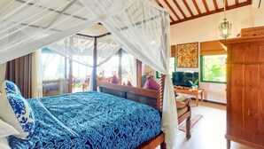 A bedroom with a canopy bed, a wooden headboard, a television, a wooden cabinet, and a view of the outdoors. - Kampung Kecil Front Beach  (Kubu)