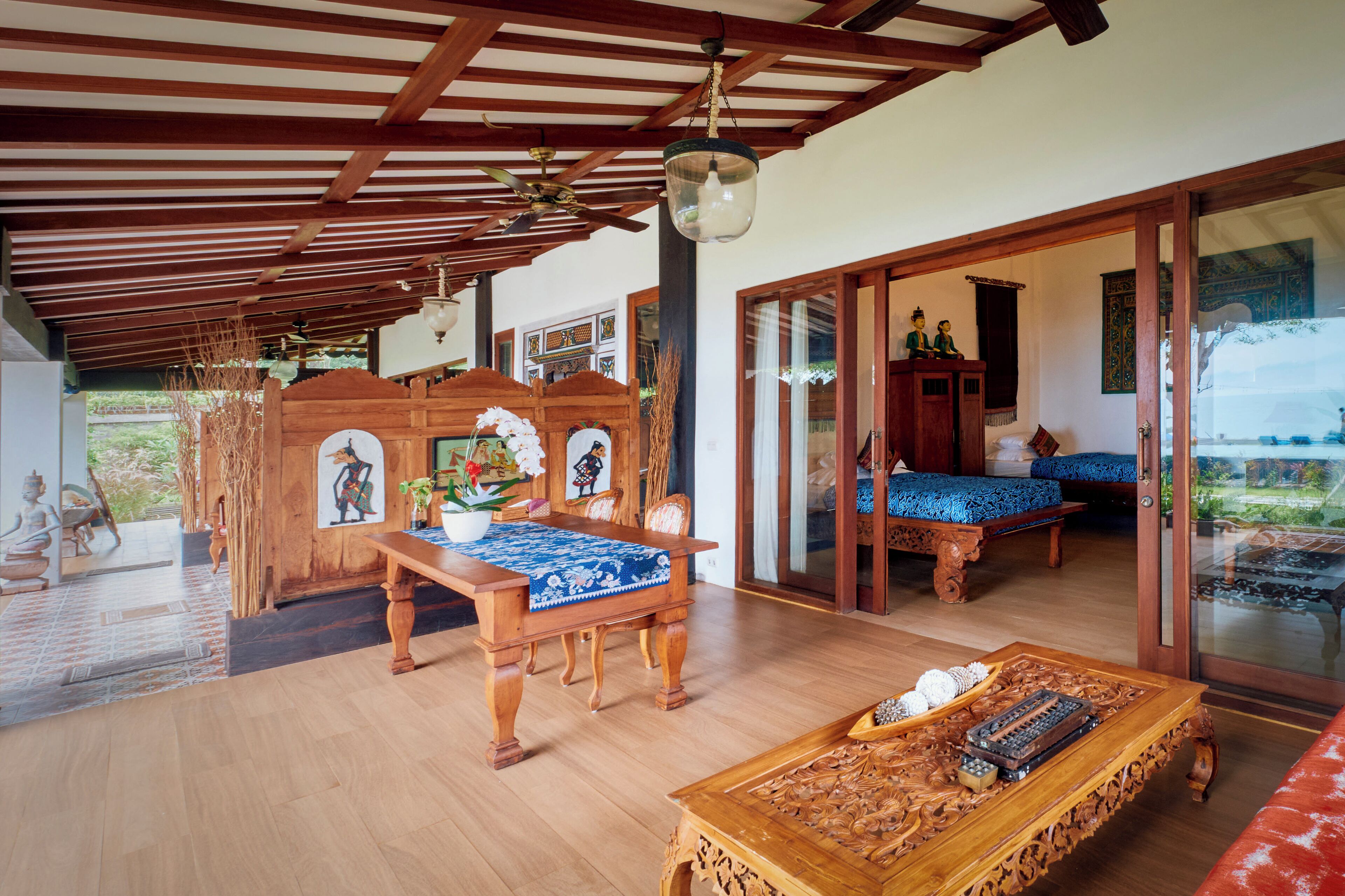 A traditional wooden interior with a dining table, a sofa, and a decorative wooden table with intricate carvings.