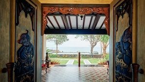An entrance with ornate carvings and a view of a garden and sea. - Kampung Kecil Front Beach  (Kubu)