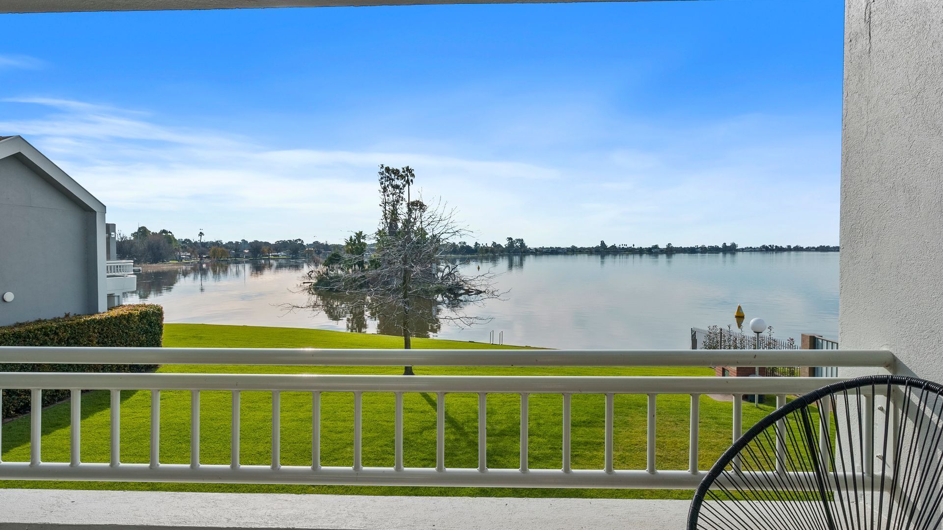 A balcony with a view of a lake, a grassy area, and a building.
