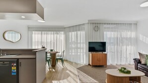 Ein modernes Wohnzimmer mit Flachbildfernseher, einem Essbereich mit Stühlen und einer Küche mit Kühlschrank.