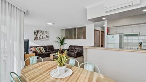 A modern living room with a dining table, two sofas, and a kitchen area with a refrigerator and cabinets. - Yarrawonga Lakeside Apartment 48 (Mulwala)