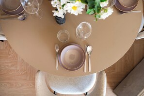 Una mesa redonda con mantel beige, un florero con flores blancas y una planta pequeña en maceta.