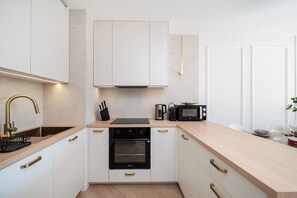 Una cocina moderna con armarios blancos, un lavaplatos de acero inoxidable, un microondas y un horno empotrado.