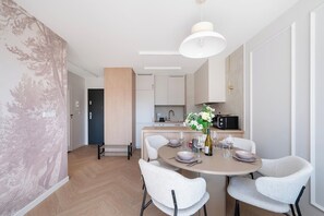 A modern kitchen with white cabinets, a black microwave, and a dining area with a round table and four chairs. - Downtown Apt - Parking, Balcony, Top Location - by Rentujemy (Łódź)