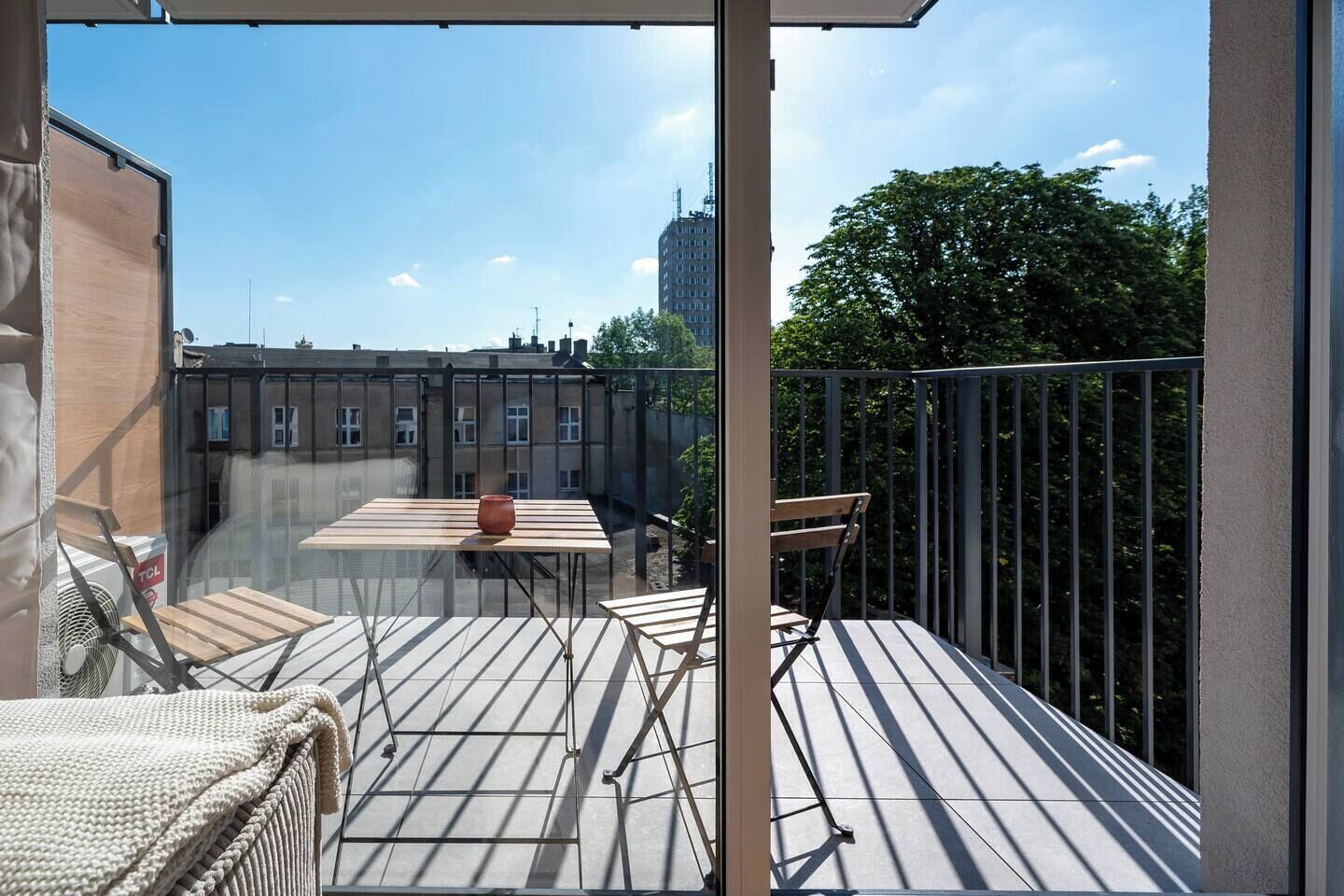 Un balcon avec une table et des chaises, un plancher en bois et une vue sur les bâtiments et les arbres.