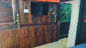 A room with a wooden wall, a television mounted above a window, and a bed with a blue mattress. - Celestial forest (Provincia de Alajuela)