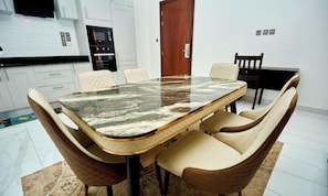A modern dining area with a marble table, leather chairs, a kitchen in the background, and a wooden door. - 2-bedroom apartment in fantastic Accra at Arlington court (Accra)