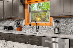 A kitchen with marble countertops, a built-in sink, a window with a view of greenery, and a blender. - Pool Cabin with 5 King Bedrooms (Cosby)